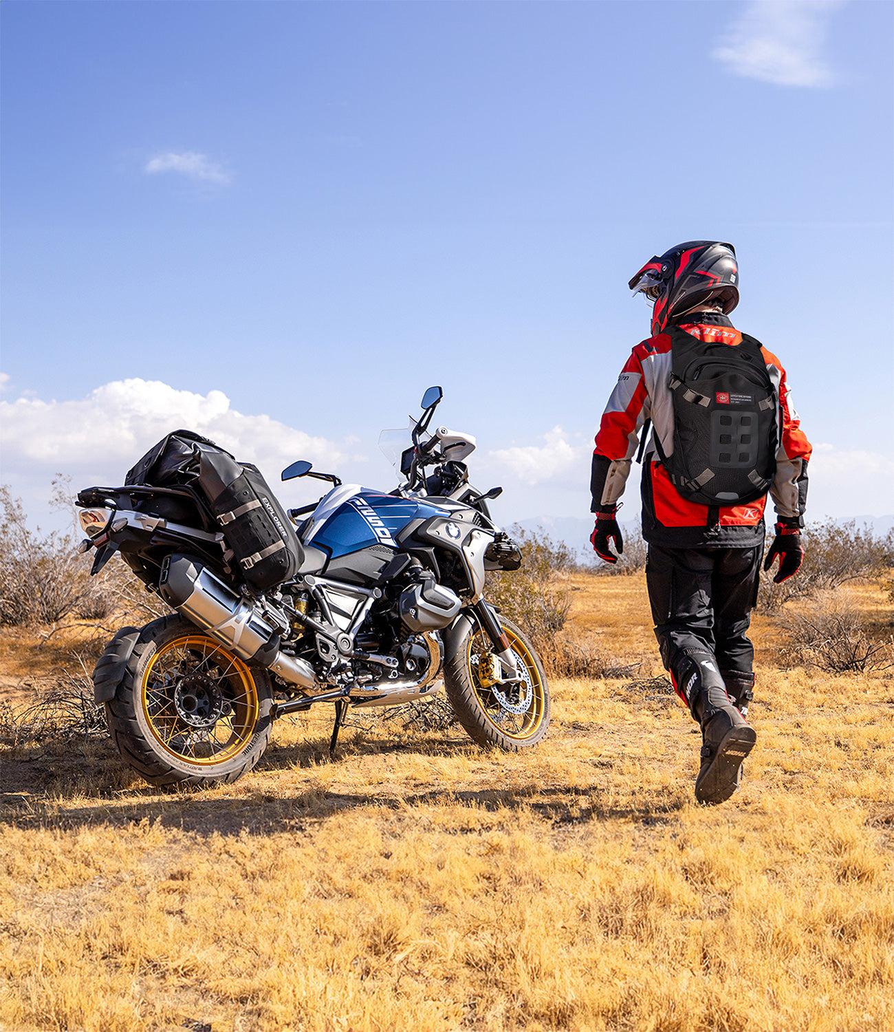 Adventure motorcycle rider wearing a waterproof hydration bag near touring bike in off-road terrain