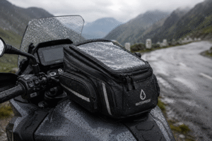 Close-up of a waterproof motorcycle tank bag attached to an adventure bike on a rainy mountain road.